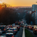 Sunset view of a busy city street filled with cars in a long traffic jam, showing the warm glow on vehicles and buildings .