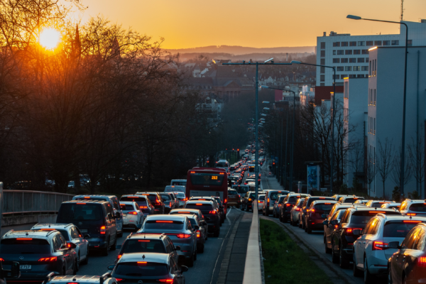 Sunset view of a busy city street filled with cars in a long traffic jam, showing the warm glow on vehicles and buildings .